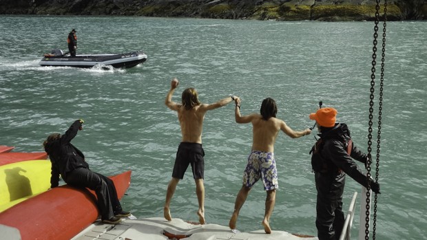 2 young boys jumping into the Alaskan water with a skiff motoring in front of them.