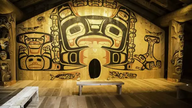 A Tlingit house with large totem art on the walls and poles.