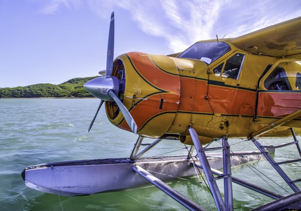 A yellow and orange Alaskan float plan sitting on the water in Alaska.