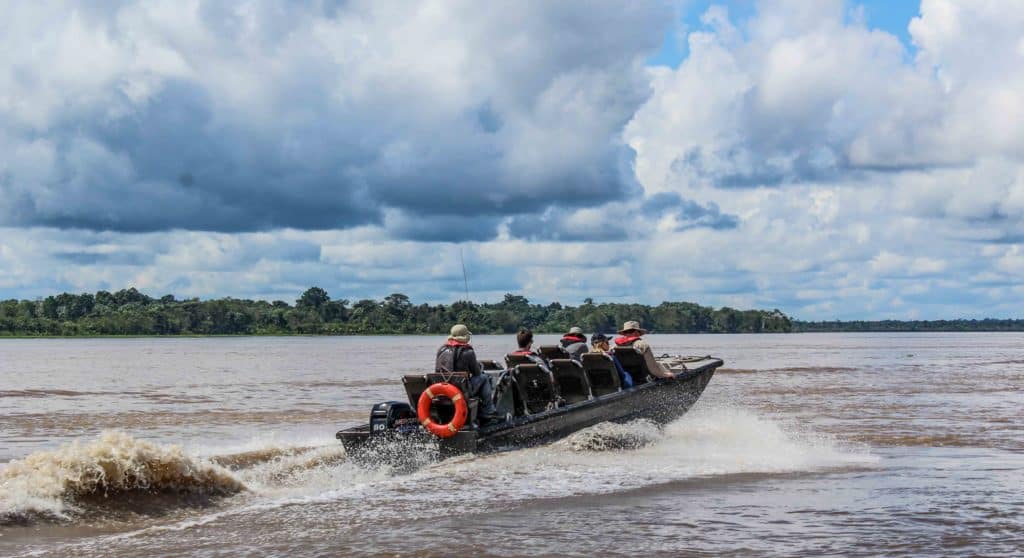 A skiff tour in the Amazon in wide open waters with land and clouds behind.