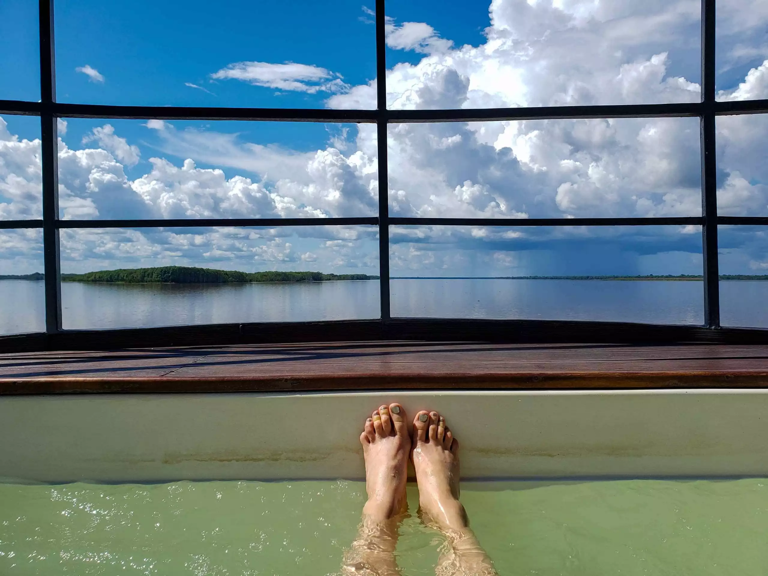 person laying in a small pool off a river cruise in the amazon with blue skys and white fluffy clouds