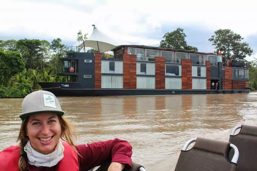 Adventure Specialist Taylor Cranney smiling on a skiff in front of the Aria cruise ship in the Peruvian Amazon.