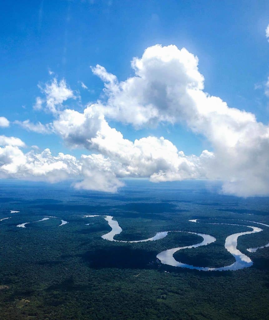 The Peruvian Amazon from above winding along through dense forest and fluffy clouds.
