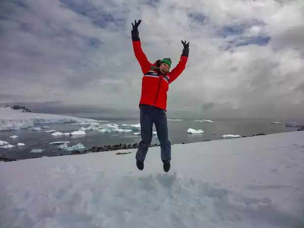 Happy guest from a small ship cruise stepping foot on land in Antarctica and jumping with her arms up. 
