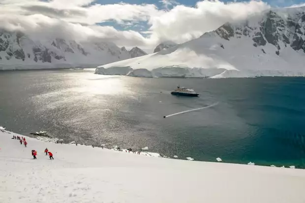 Guests hiking on snow with their small ship in the background in Antarctica. 
