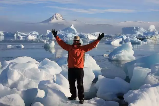 Small ship cruise guest posing with many icebergs behind him while on land tour in Antarctica from small ship cruise. 