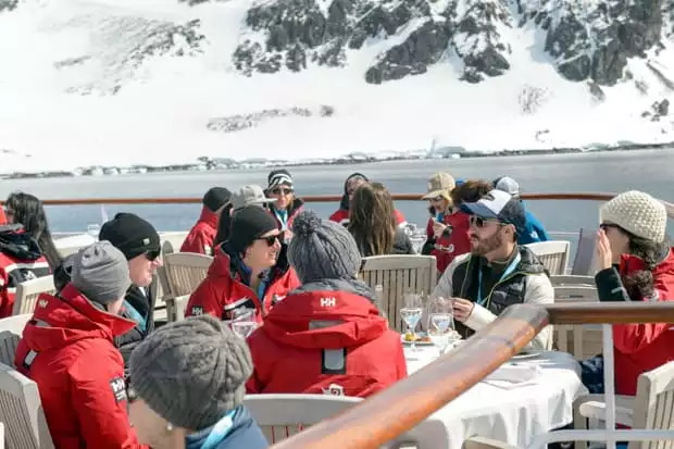 Guests aboard a small ship cruise in Antarctica enjoying the sun, food, and drink on the deck. 