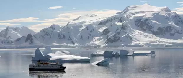 View of small expedition cruise ship in Antarctica surrounded by glaciers and snowy peaks. 