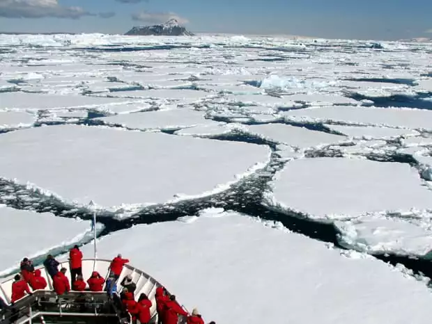 Guests on the bow of a small ship expedition cruise in Antarctica as the ship is breaking through the ice on the water. 