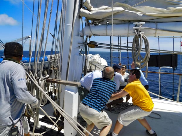 Galapagos passengers on the small ship sailing cruise Mary Anne helping to hoist the sails on the boat with crew.