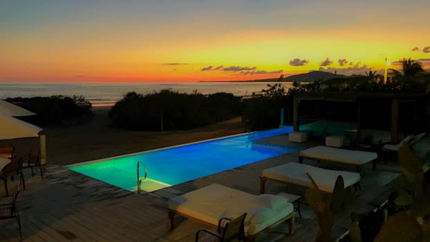 Yellow and orange sunset from a lodge with a pool and lounge chairs.