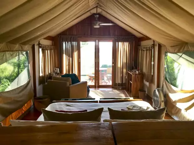 View from the inside of a safari tent camp with a couch, open air netted windows, chair and sliding glass doors on a Galapagos land tour.