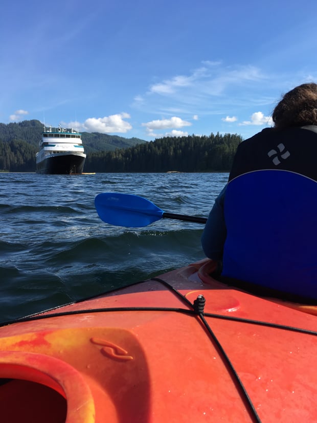 Guests kayaking in front of their small cruise ship in Alaska. 