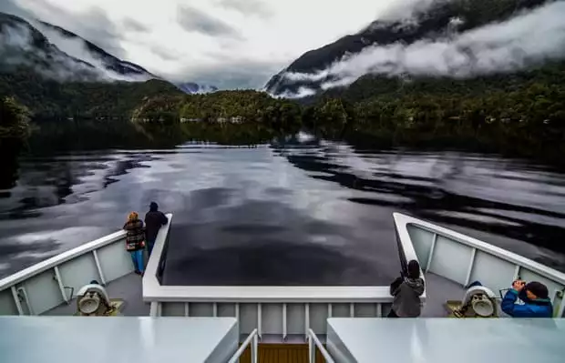 View from the stern of a small ship cruise going through misty fjords in New Zealand.