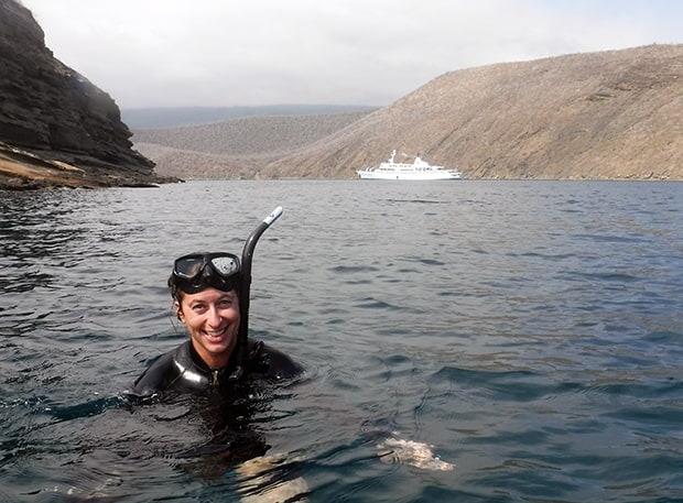 Happy traveler snorkeling in the Galapagos Islands with the small ship cruise Galapagos Legend anchored in the background.