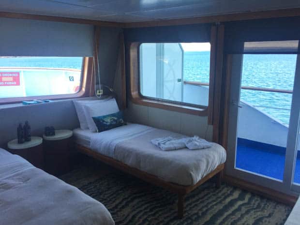 Stateroom view of 2 twin beds with large panoramic windows and sliding glass door on the small ship cruise Galapagos Legend.