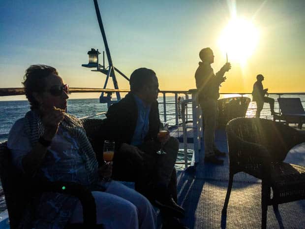 Small ship cruise travelers on the deck of the Galapagos Legend outside for sunset.