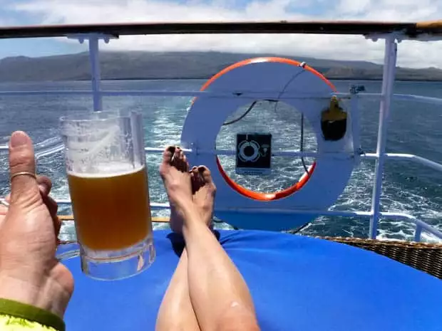 Stern of the boat with a happy traveler lounging on a chair enjoying a beer while the Galapagos Legend sails away from a Galapagos Island.