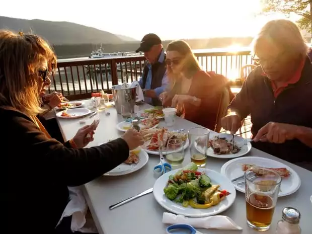 Guests from a small ship cruise in Alaska eating a seafood dinner at Orca Point Lodge along the water during sunset. 