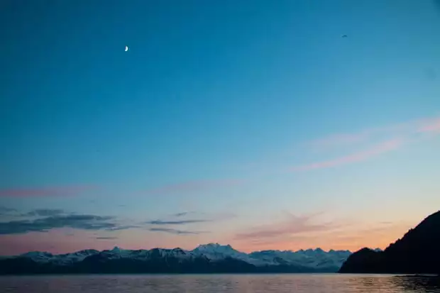 Moon above the mountains in Alaska during sunset as seen from a small ship. 