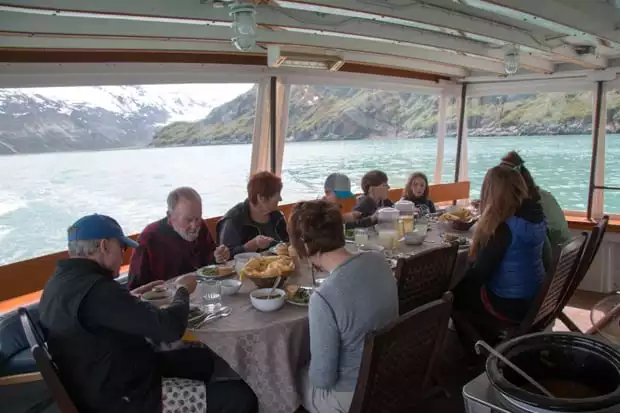 Guests eating dinner aboard the Sea Wolf surrounded by windows while scenic cruising in Alaska. 