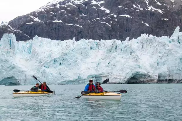 Guests from a  small ship cruise in double kayaks paddling in front of a glacier in Alaska. 