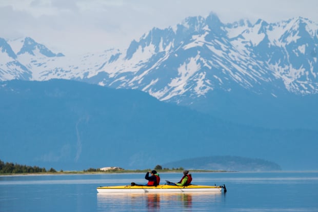 Guests from a small ship cruise  in Alaska kayaking with mountain peaks in the background. 