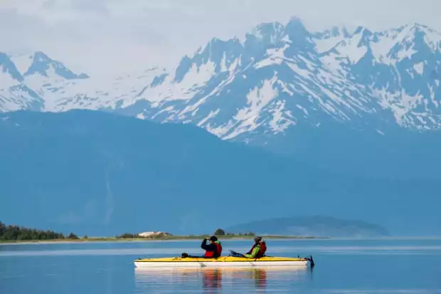 Guests from a small ship cruise  in Alaska kayaking with mountain peaks in the background. 