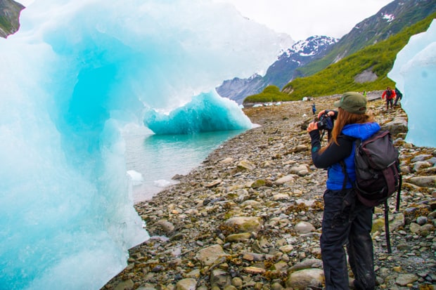 Guests on a small ship cruise tour taking pictures of bright blue ice bergs near the shore in Alaska. 