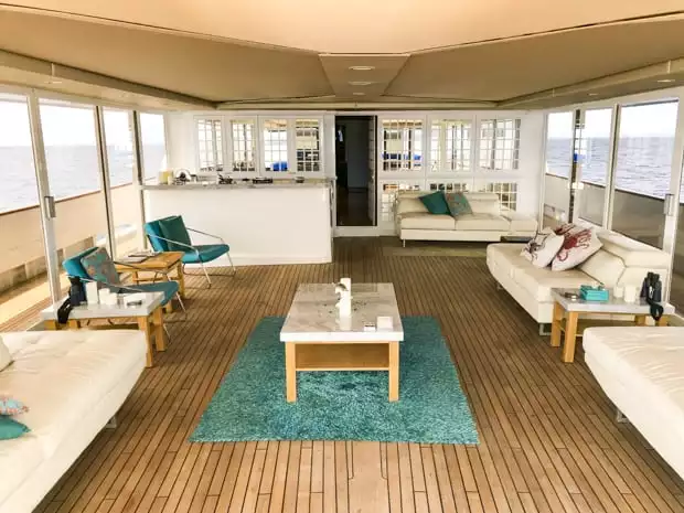 Deck view of a enclosed outdoor lounge area with couches and chairs and a bar.  Large windows and sliding glass doors access the deck.