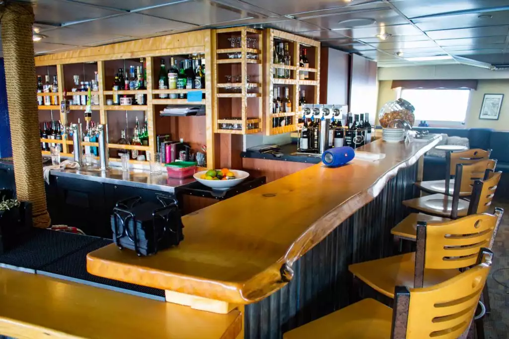 a photo of the bar aboard Wilderness Adventurer, showing glossy wooden counter tops with, wooden high chairs,  cubbyholes are full of spirits, alcohol and other beverage choices 