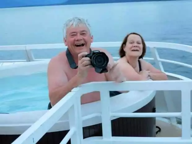 Happy guests in the hot tub on their small ship cruise in Alaska taking pictures of the scenery as they sail. 