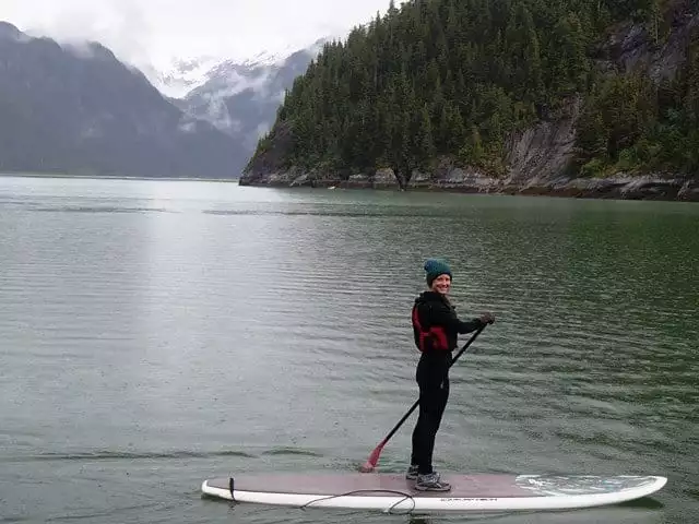 Happy guest stand up paddle boarding in calm waters from a small ship cruise in Alaska. 