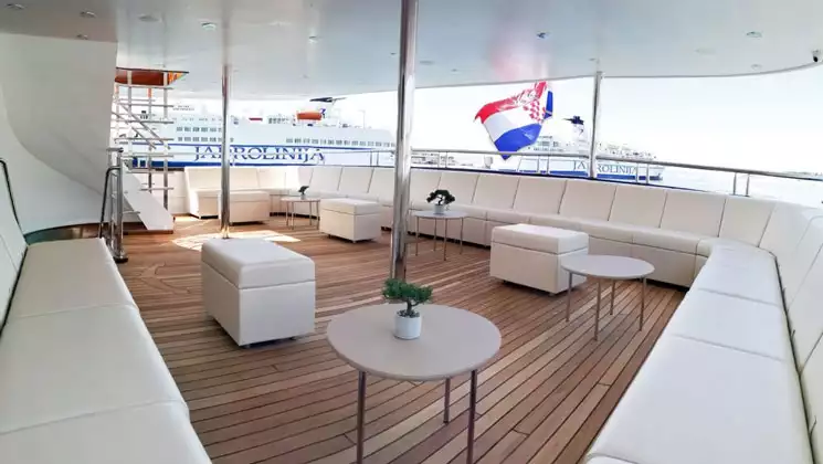 Middle-deck exterior seating area with wraparound white leather couch, teak decking & white leather ottomans, aboard Aurelia yacht.
