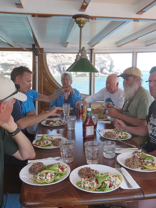 baja california small ship cruise passengers talk and eat at a table on a covered deck of the westward