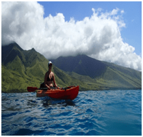 Kayaker in Hawaiian blue waters with green mountains behind