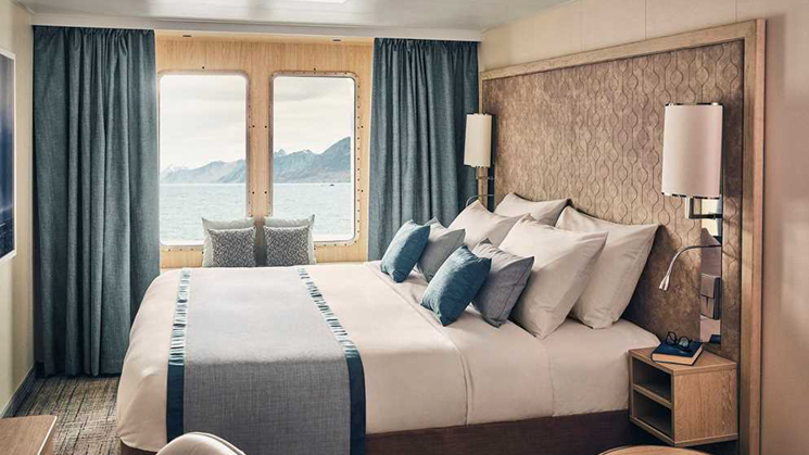 Window Suite with a large comfortable bed, two large windows aboard National Geographic Resolution polar expedition ship.