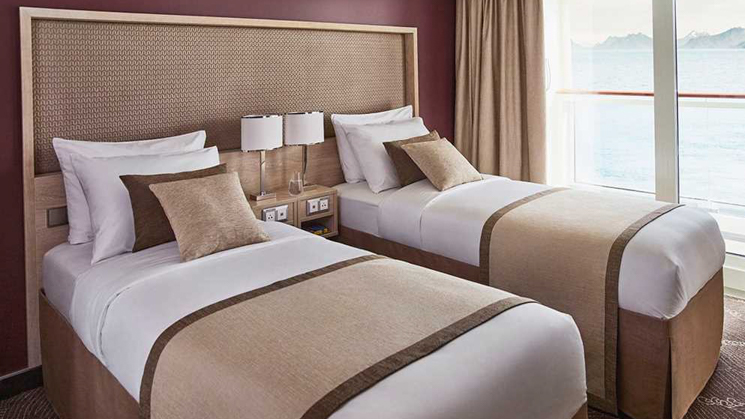 Two single beds with a shared nightstand and individual reading lights. The white duvets are accented with cream and brown.