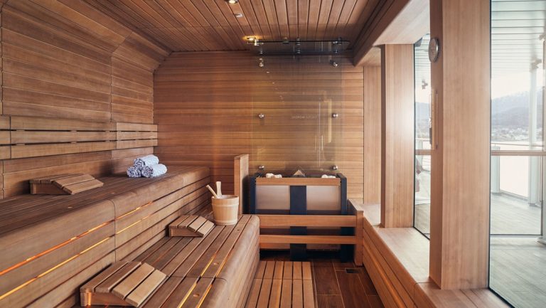 Interior of wooden sauna with 2 benches, hot rocks, water bucket with ladle & large view windows on Nat Geo Resolution.