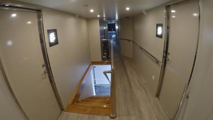 Hallway on yacht Rhapsody with shiny beige walls, wood staircase, light-up cabin numbers & recessed lighting.