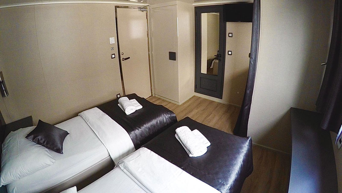 Lower Deck cabin on yacht Rhapsody with 2 twin beds, beige walls, natural light from a window, mirrors & black-&-white bedding.