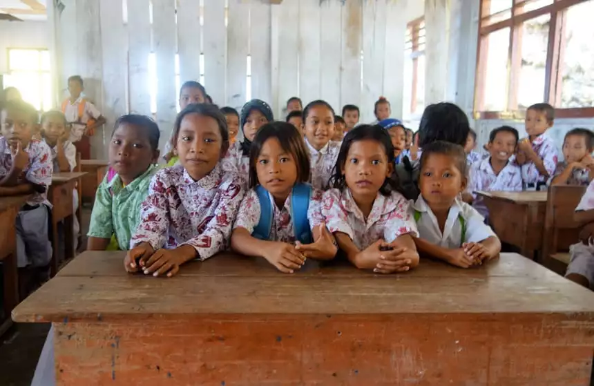 Indonesia children sitting at a wooden school desk in their patterned uniforms.