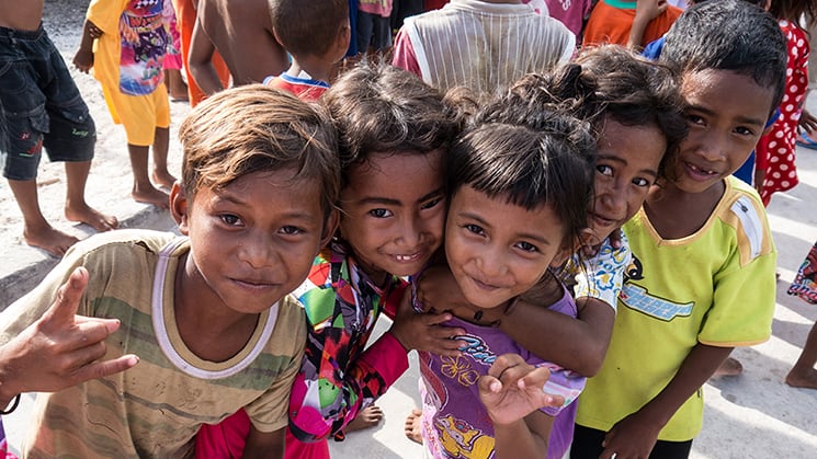Village children leaning in and smiling for the camera in Sulawesi, Indonesia.