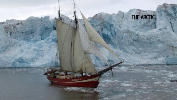 A small ship with its sails down in front of an iceberg