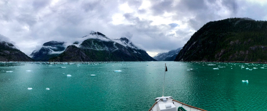 bow of ship cruising into scenic mountain vista and teal waterway on alaska small ship cruise