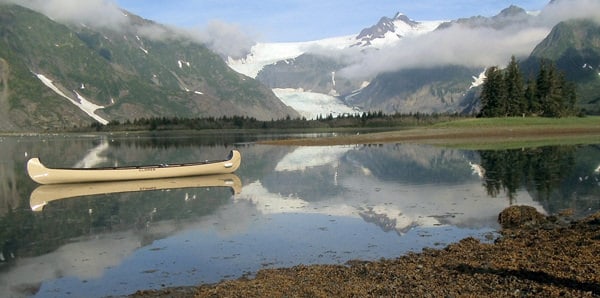 Kenai Glacier Lodge Canoe on a glassy lake with Pederson Glacier in the background.