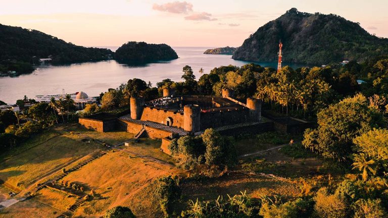 Fort Belgica glows during golden hour sunset towering on a small hill of Neira Island in Indonesia not far from the ocean.