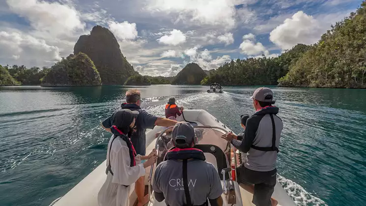 Guests on Aqua Blu Raja Ampat Cruise take a tender boat to explore turquoise sea & green gumdrop islands in Indonesia.