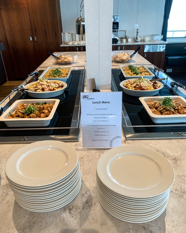 Lunch buffet set up aboard Coral Adventurer Australia small ship. Two sides of a granite counter top with white serving bowls of food offerings, a white menu printed with two stacks of plates