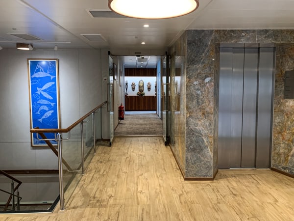 Elevator aboard Coral Adventurer, light wooden floor with stone granite walls and a silver metal elevator